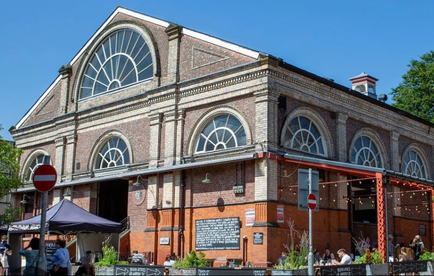 Brick building with large windows and outdoor seating area on a sunny day
