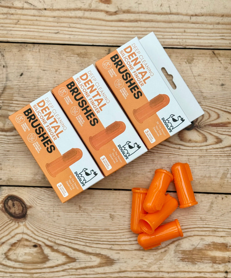 A set of five orange dog finger toothbrushes with packaging, displayed on a wooden surface.