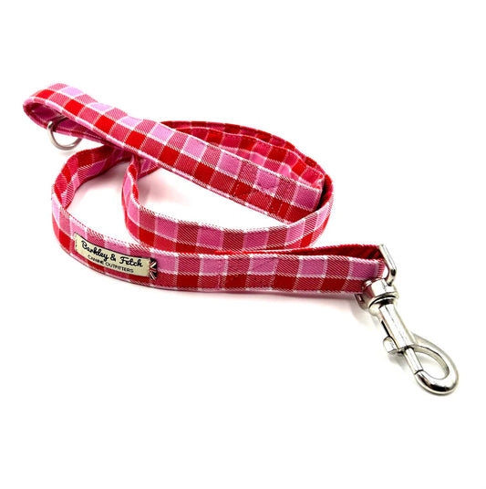 A pink and red checkered dog lead with a comfortable loop handle, an accessory attachment ring, and a strong steel trigger clip.
